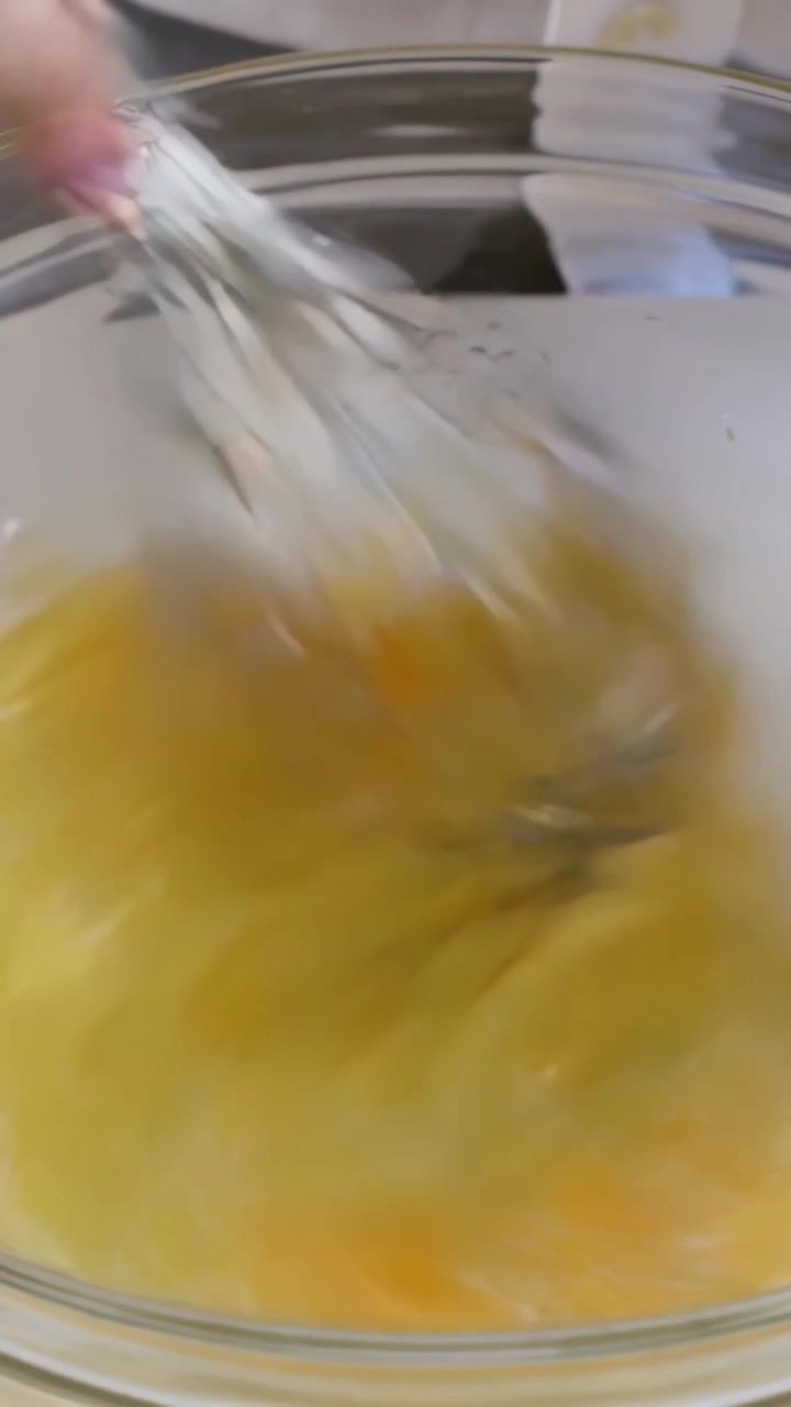 Video verticale: Mano che entra e sbatte uova crude per una frittata in una ciotola con una frusta sul bancone.
