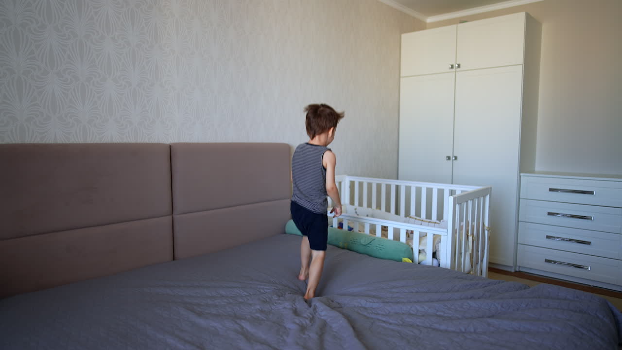 Healthy active toddler boy jumping on the bed. Happy kid goes to his crib and gets there.