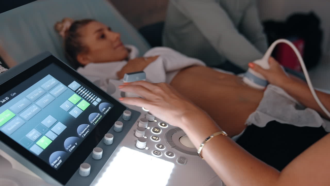 Doctor's hand operating ultrasound machine for pregnant lady examination. Medic moves the sensor by the belly of Caucasian woman.