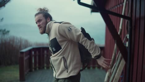 Bearded-Man-With-Backpack-Is-About-To-Leave-His-Cottage-On-Windy-Day