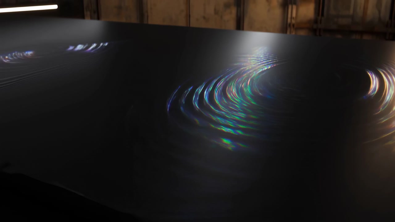 A closed black laptop rests on a rough wooden surface inside a dim industrial workspace, with soft reflections on the matte lid and warm ambient light in the