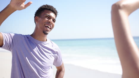 a young biracial man with curly hair, wearing a purple shirt, smiles joyfully on a sunny beach