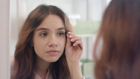 attractive girl plucking eyebrows on face with tweezers front mirror at bathroom