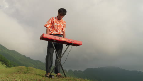 low to earth shot of a man playing the piano in the wind on a mountaintop