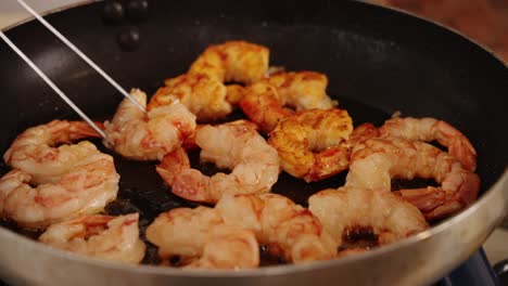 close up shot of tasty fresh prawns browning in a saute pan in slow motion, with chef using tongs to flip the prawns