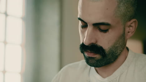 close-up face of a thoughtful, serious, and focused handsome bearded caucasian young male businessman working at home office, writing plans, thinking, and brainstorming ideas