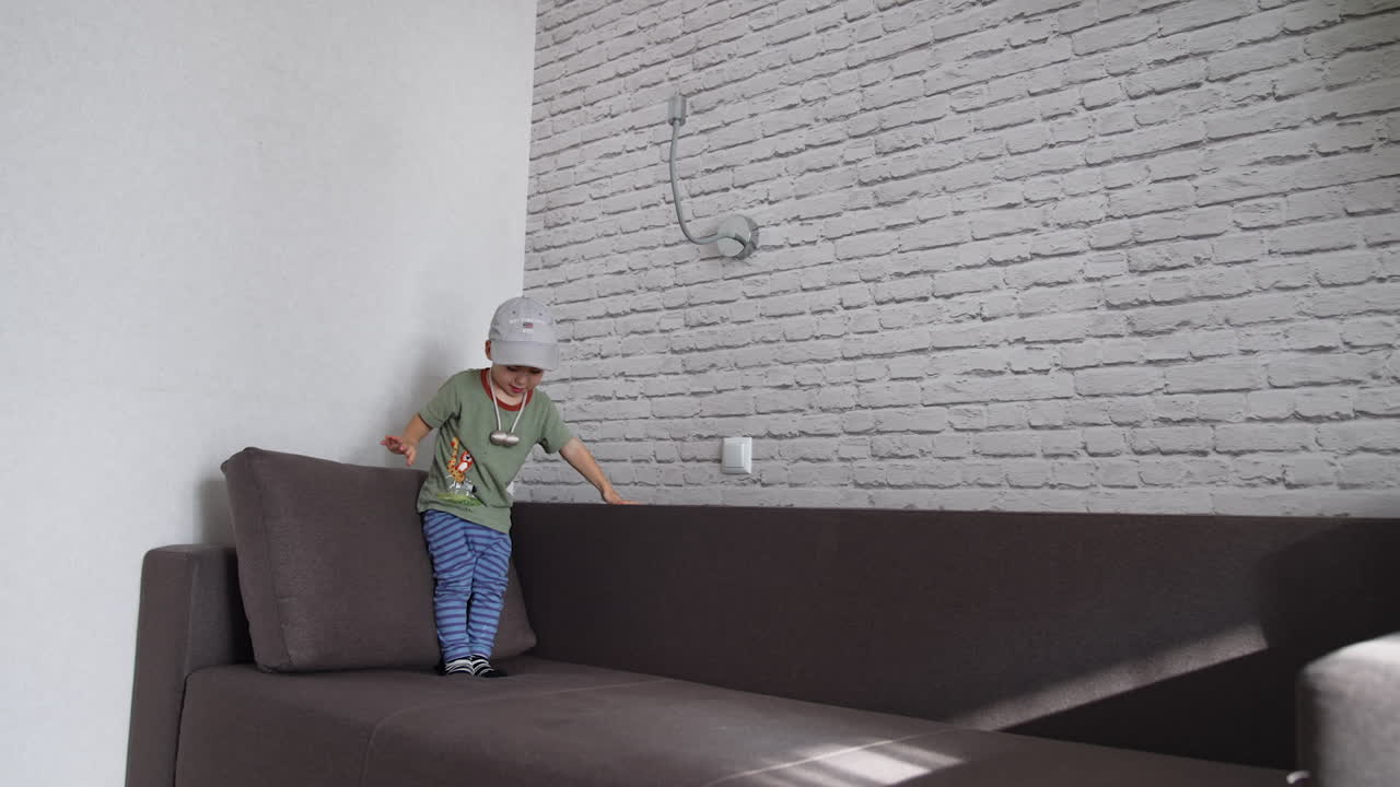 Caucasian toddler boy having fun time at home. Energetic active healthy baby boy jumping on the big sofa.