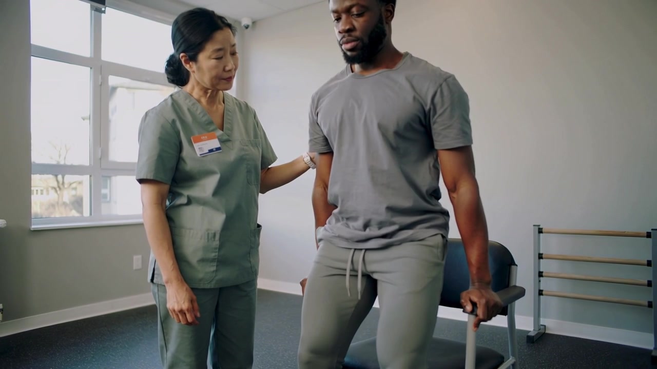 Standing patient after caregiver scrubs placing hand, pushing on armrests in rehab for balance