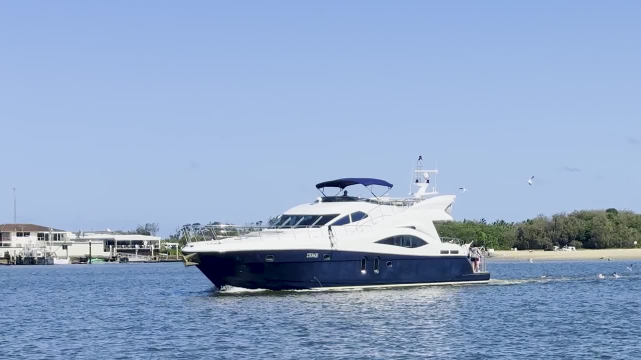 A luxurious yacht cruises smoothly near coastal homes under a clear blue sky.
