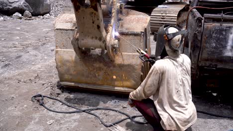 unrecognizable worker repairing excavator by welding bucket to arm