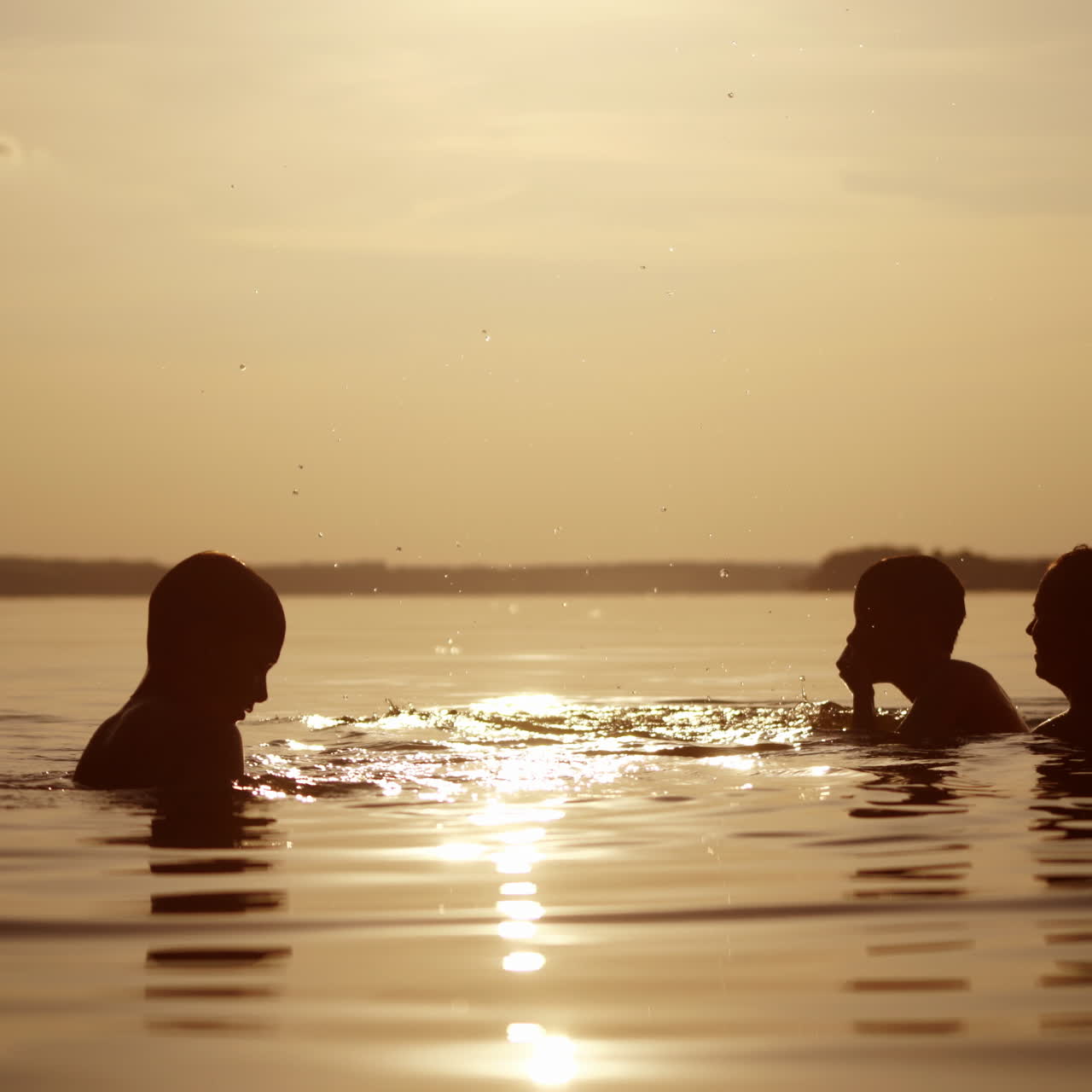 Woman and two children playing in water in the evening. Silhouette of female and boys having fun in the river at sunset. Mother throws up her son into the water.