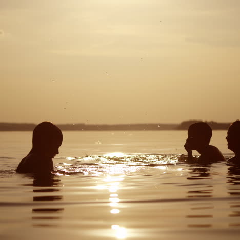 woman and two children playing in water in the evening. silhouette of female and boys having fun in the river at sunset. mother throws up her son into the water.