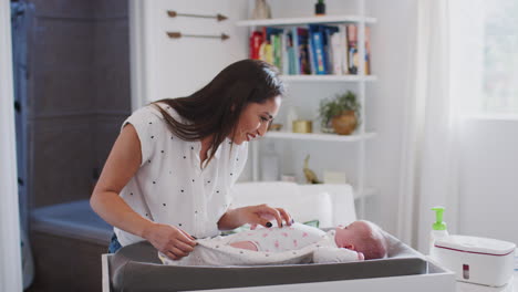 madre feliz cambiando el pañal de su hijo recién nacido en casa en una mesa de cambio de bebé, cintura hacia arriba