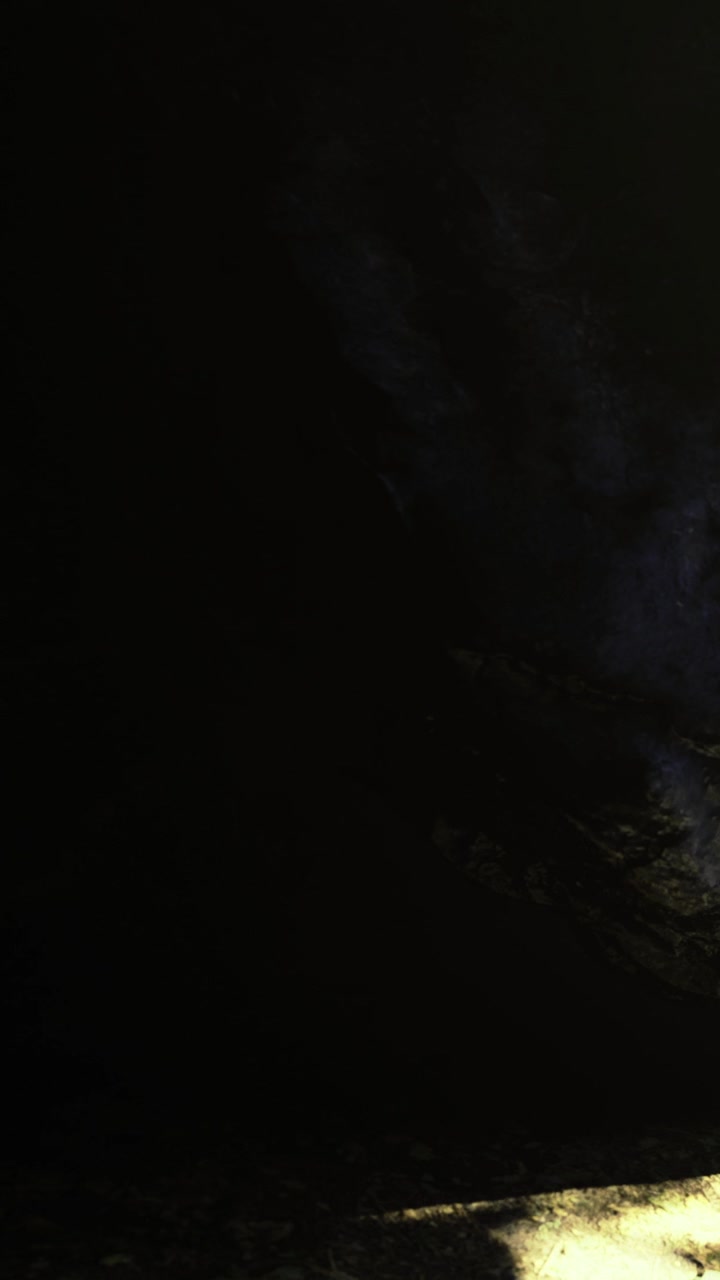 Cena de caverna escura com luz fraca iluminando superfície rochosa e sombras.