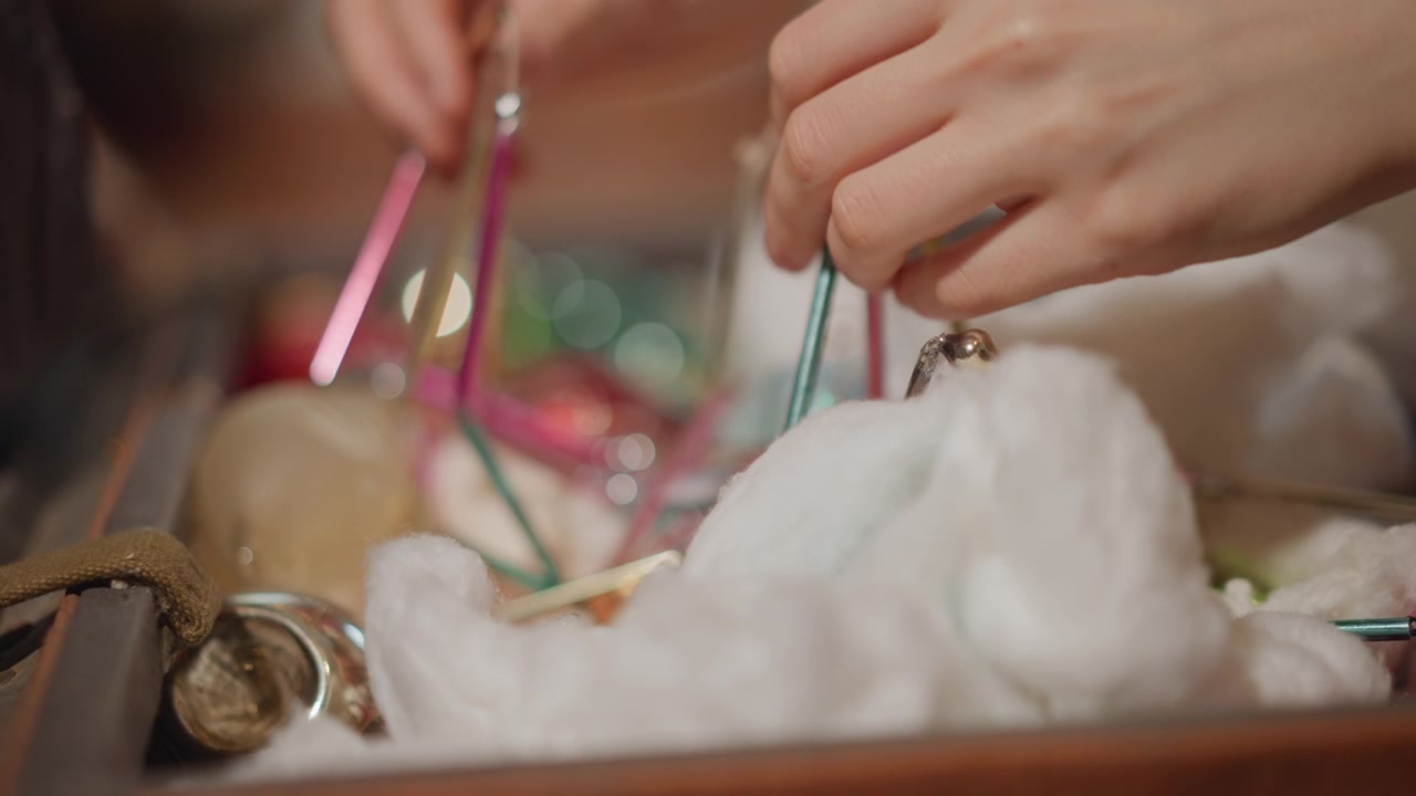 Mani che sistemano ornamenti vintage in una scatola imbottita, una donna caucasica dispone ovatta, ganci e palline per una conservazione sicura, posizionando con cura fragili decorazioni in vetro, in una preparazione stagionale ordinata e dall'atmosfera calda.