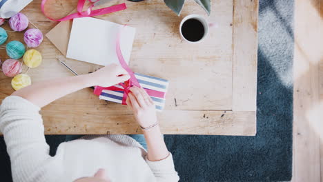 disparo de arriba mirando hacia abajo a la mujer en casa escribiendo en una tarjeta de cumpleaños y envolviendo un regalo