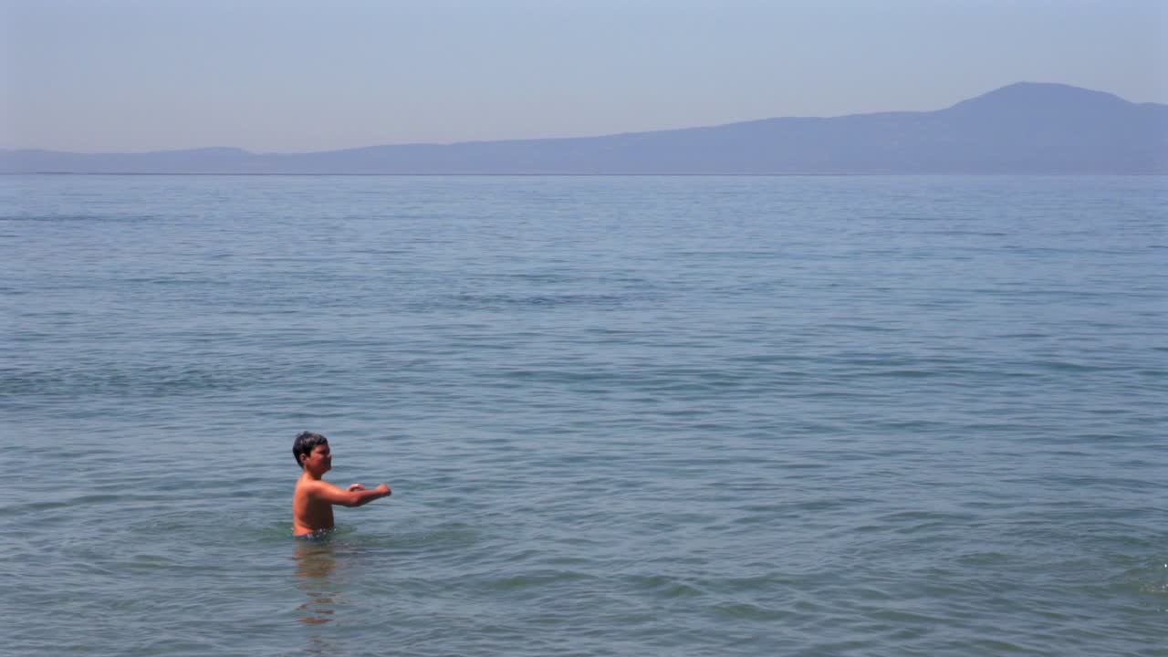 Slow motion 100fps footage of two caucasian brothers , playing with a small beach ball at sea of Kalamata , medium, static shot