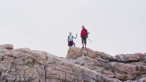 senior hiker couple with backpacks and hiking poles standing with their arms wide open on the rocks