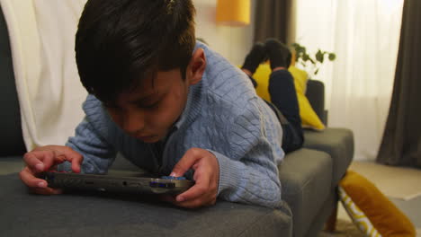 niño acostado en el sofá en casa jugando a un juego o transmitiendo a un dispositivo de juego portátil 5