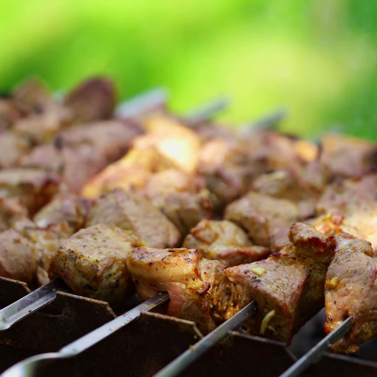 Delicious kebab outdoors. Preparation of pork meat on grill. Skewers with barbecue in mangal on green background.