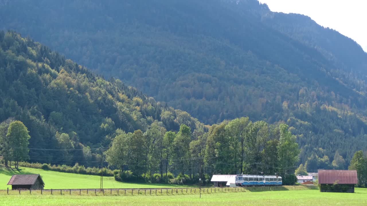 pequeño tren azul conduciendo por el ferrocarril junto al prado verde en la zona alpina