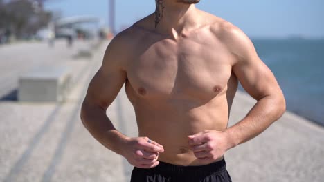 cropped shot of shirtless sportsman running at riverside