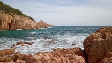 Slow-motion-panoramic-calm-turquoise-ocean-waters-breaking-against-coastal-cliff,-mediterranean-landscape-with-clear-skyline