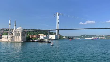 footage of boats passing on bosphorus, historical landmark called "ortakoy mosque" and bridge in istanbul. it is a beautiful scene in a sunny summer day.