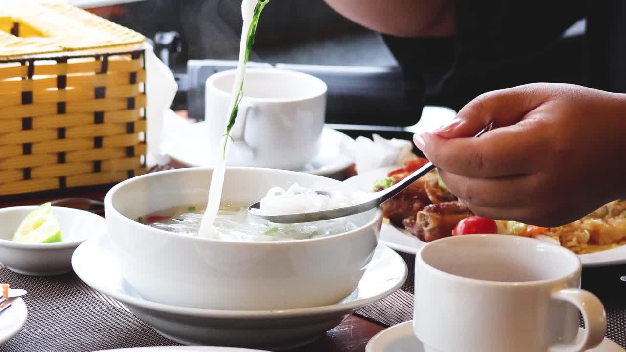 Using chopsticks to transfer pho to a spoon