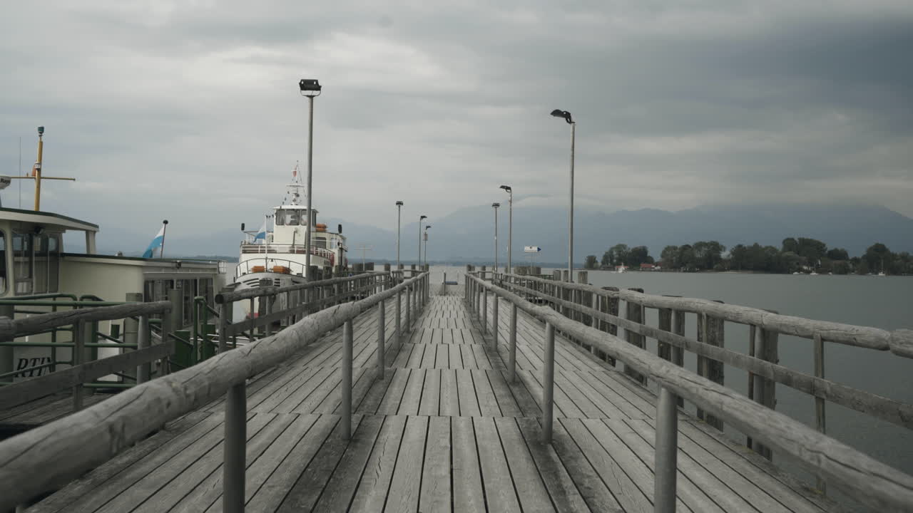 Steady shot of two boats waiting for passengers to carry to the next port at the lake Chiemsee (barvarian sea) in the morning on a cloudy day with cloudy mountains in the background