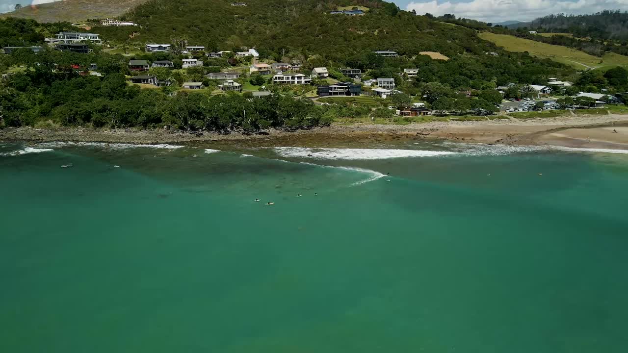 panorámica aérea cinematográfica sobre los surfistas esperando en la fila para que rompa la próxima ola en la pequeña ciudad de nueva zelanda