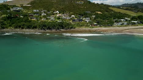 Panorámica-Aérea-Cinematográfica-Sobre-Los-Surfistas-Esperando-En-La-Fila-Para-Que-Rompa-La-Próxima-Ola-En-La-Pequeña-Ciudad-De-Nueva-Zelanda