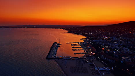 Beautiful scenery of the resort city a dusk time. Drone footage over the yacht club near the sea coast. Stunning orange sky at backdrop