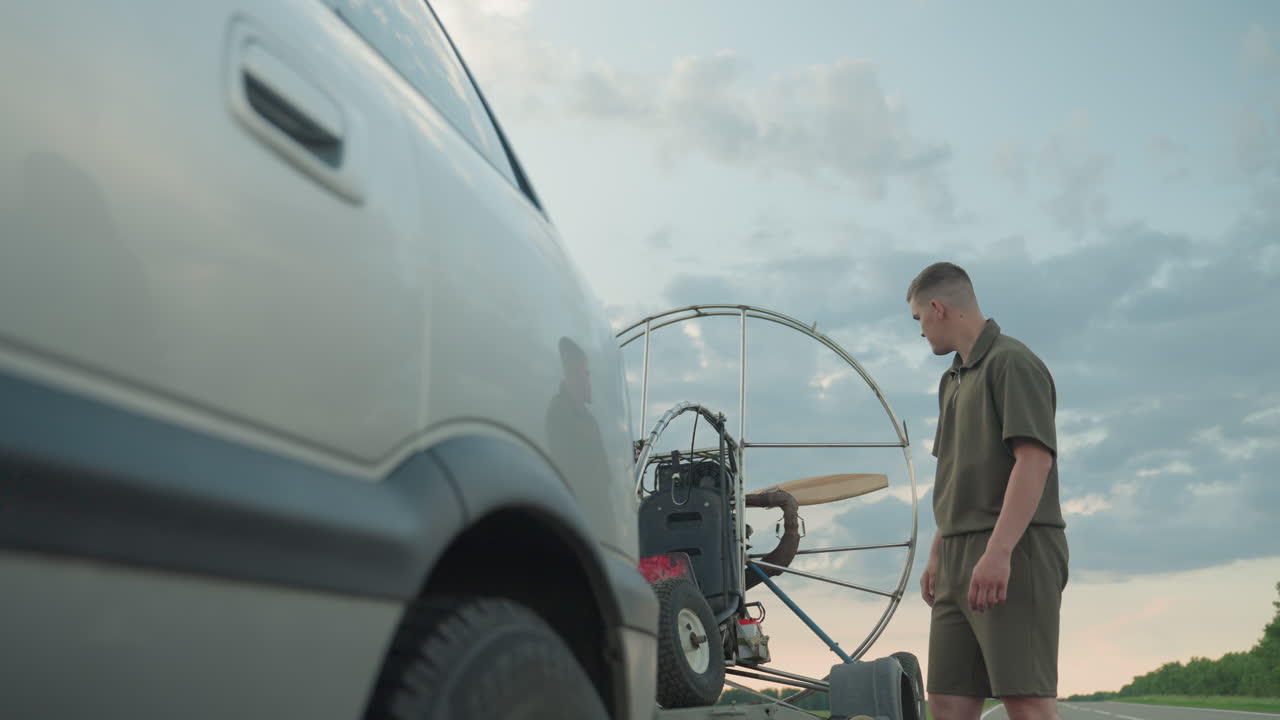 close up of man hand touching metal cage structure of paramotor with wooden propeller and sky background, focus on tactile contact and curiosity gesture