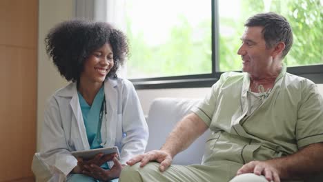 african american female medical doctor using digital tablet explain the symptoms to the patient after treatment or talking with old man patient in the hospital.