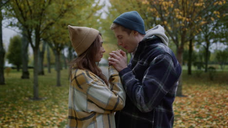 smiling handsome boy warming girls hands by blowing steam in autumn weather.