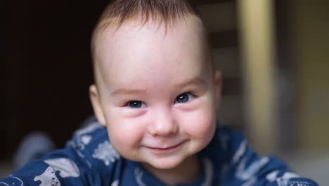 sweet adorable smile of a tiny infant kid. cheerful kind face of a little baby boy lying on his belly. close up.
