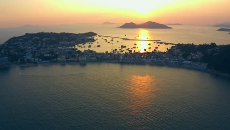drone shot traveling forward to a city build on an isthmus with a long beach all along and an harbor during a beautiful sunset