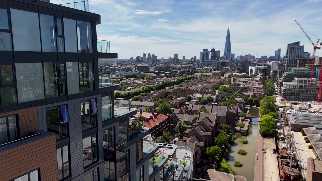 Vista dai balconi in vetro di una moderna torre di appartamenti, attraverso i tetti e un canale, verso uno skyline cittadino distante