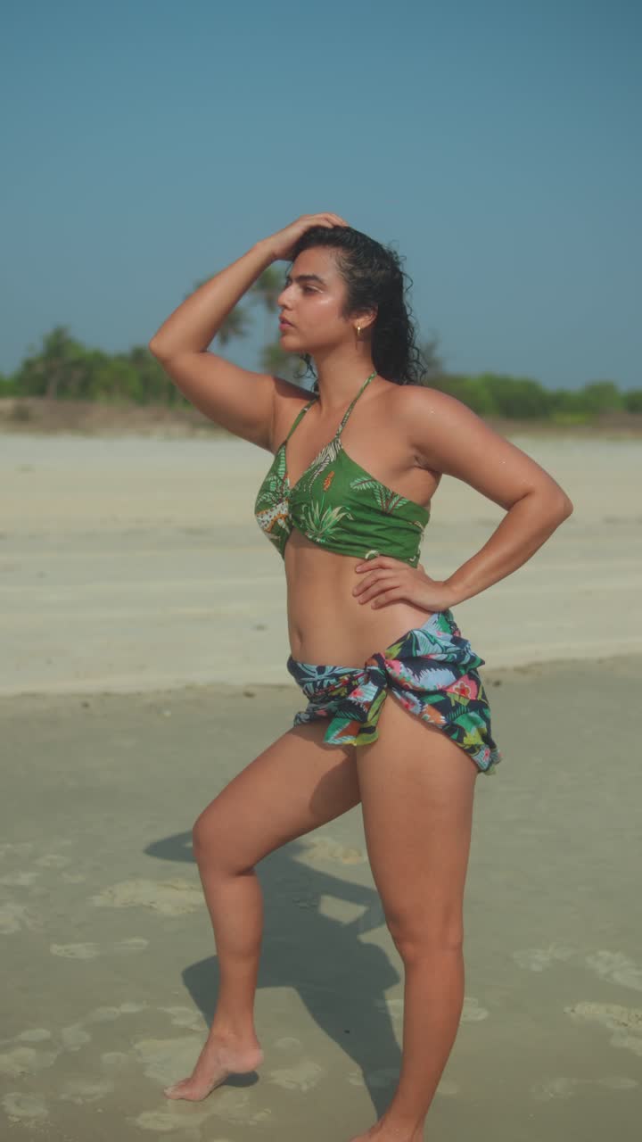 Confident woman posing on beach with tropical bikini and wrap under blue sky