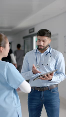 vertical video of diverse male and female doctors discussing work in hospital corridor, slow motion