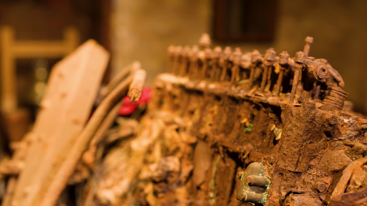 Slow camera pan reveals corroded mechanical engine part under warm lighting in historical museum setting