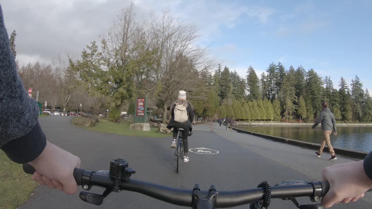 First person pov of biker hands on handlebar following friend riding bicycle in Stanley Park, Vancouver in Canada