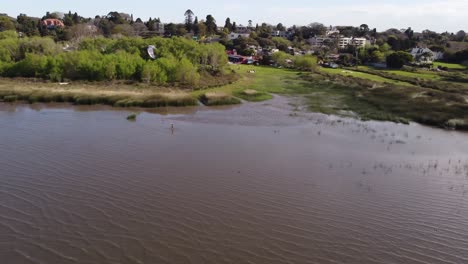 Aerial-tracking-shot-of-person-practicing-kite-surfing-in-brown-colored-river-of-Buenos-Aires-during-sunny-day