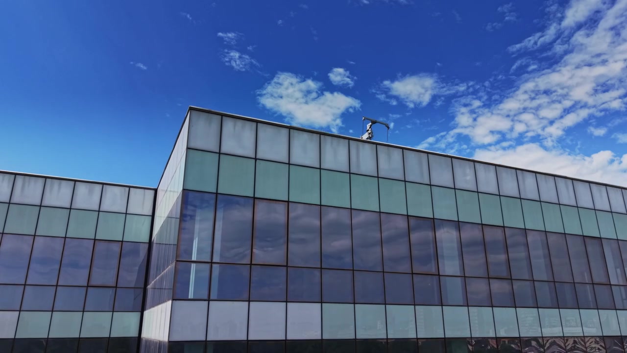 Edifício moderno com janelas de vidro refletindo nuvens e céu.