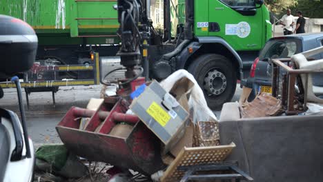 garbage truck with a mechanical arm collects waste from a pile of refuse on the sidewalk