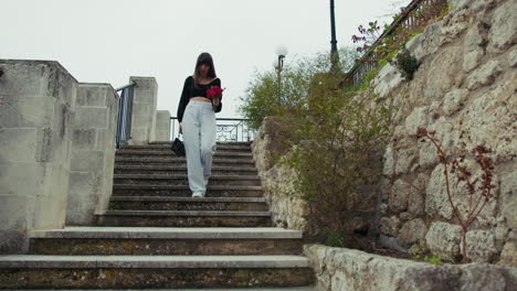 woman going down the stairs outdoor in the small town with red flowers