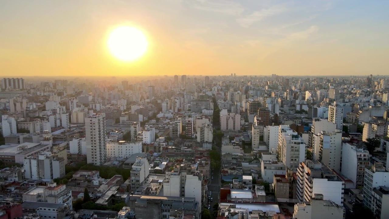 Filmagem de drone do nascer do sol sobre a cidade de Buenos Aires. Céu azul e amarelo no terço superior da tela, edifícios brancos nos dois terços inferiores. Clipe de 14 segundos.