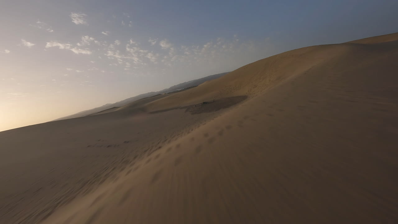 vuelo aéreo rápido y bajo sobre el agua del mar hacia las dunas de arena al atardecer, maspalomas