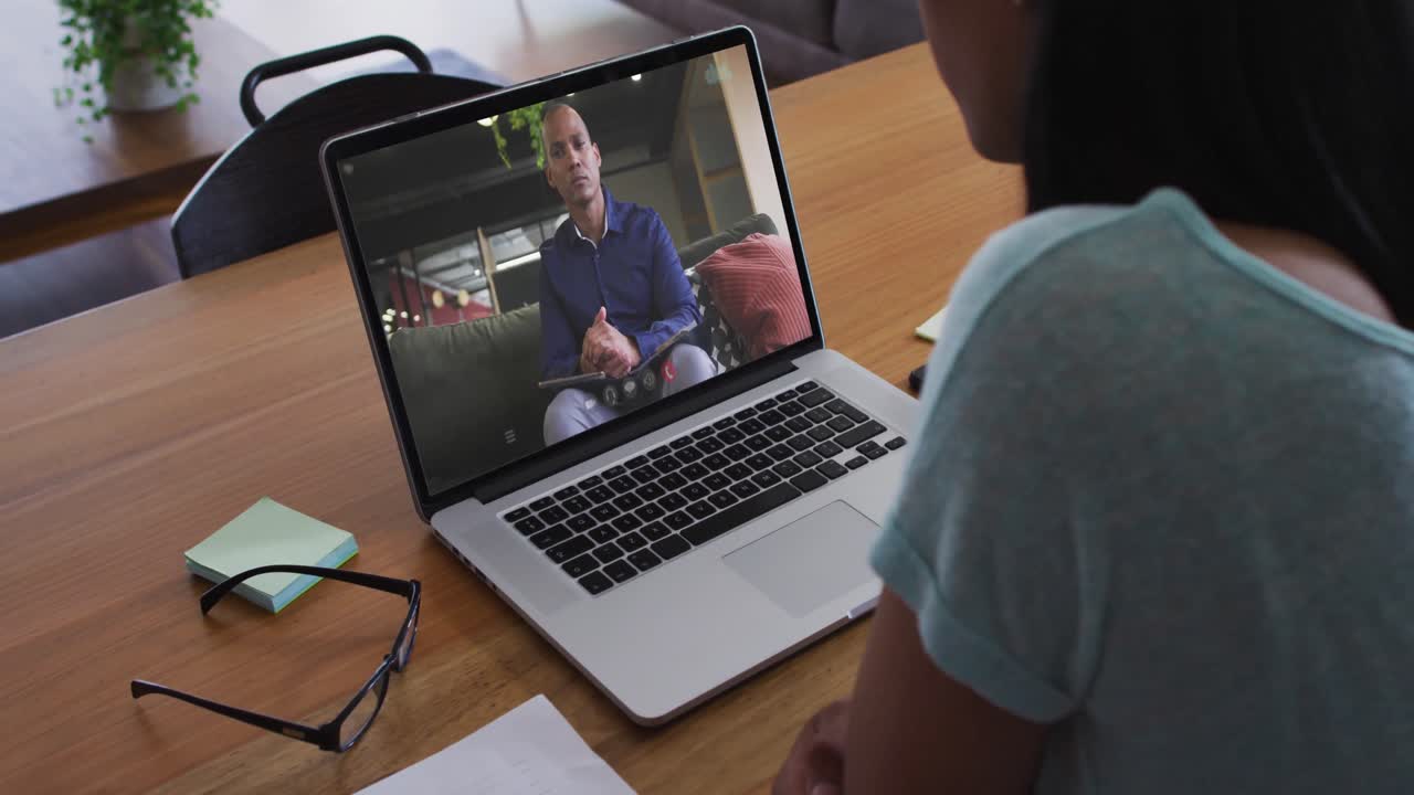 African american woman having a video call with male office colleague on laptop at home